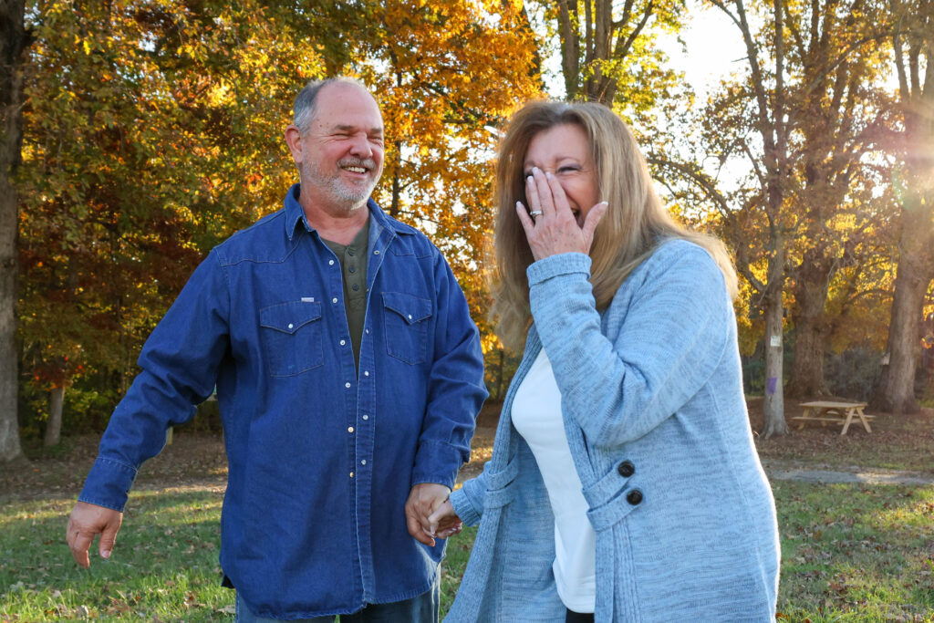 A couple in their middle age, walking through a field holding hands and laughing and smiling.