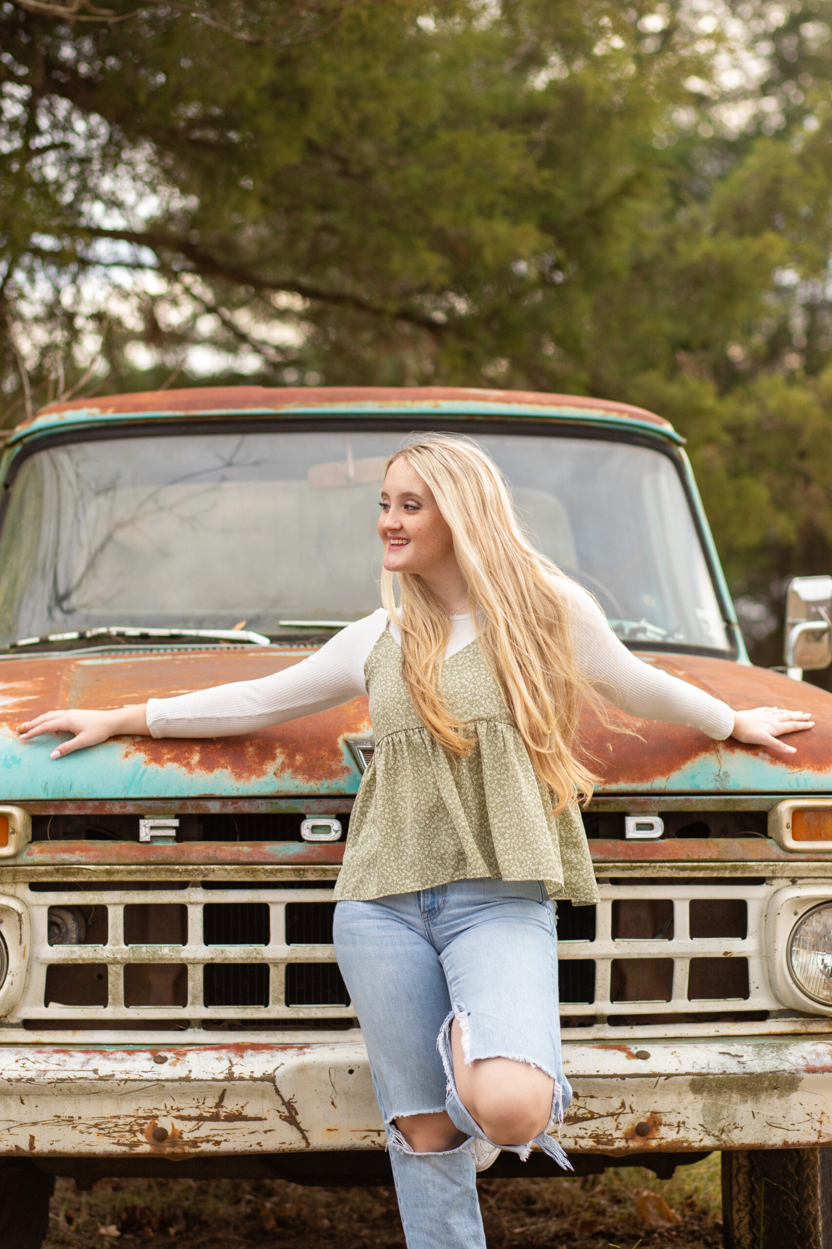 a Senior girl leans onto an old rusty truck, and looks toward her future as her long blonde hair blows into the wind