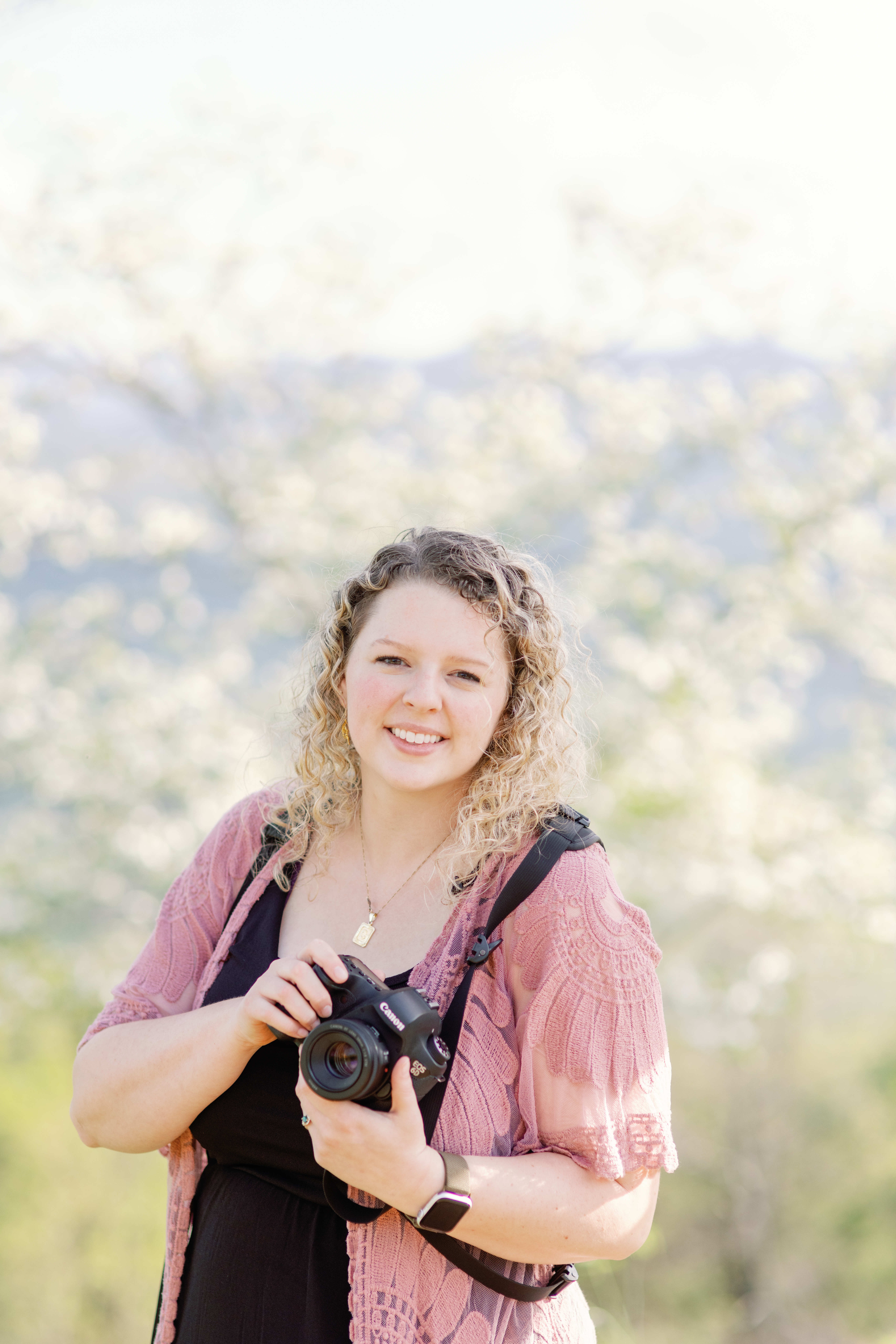Hi it's me your friendly wedding photographer carra, this is a photo of me from 2023 in the mountains of north carolina holding one of my cameras!