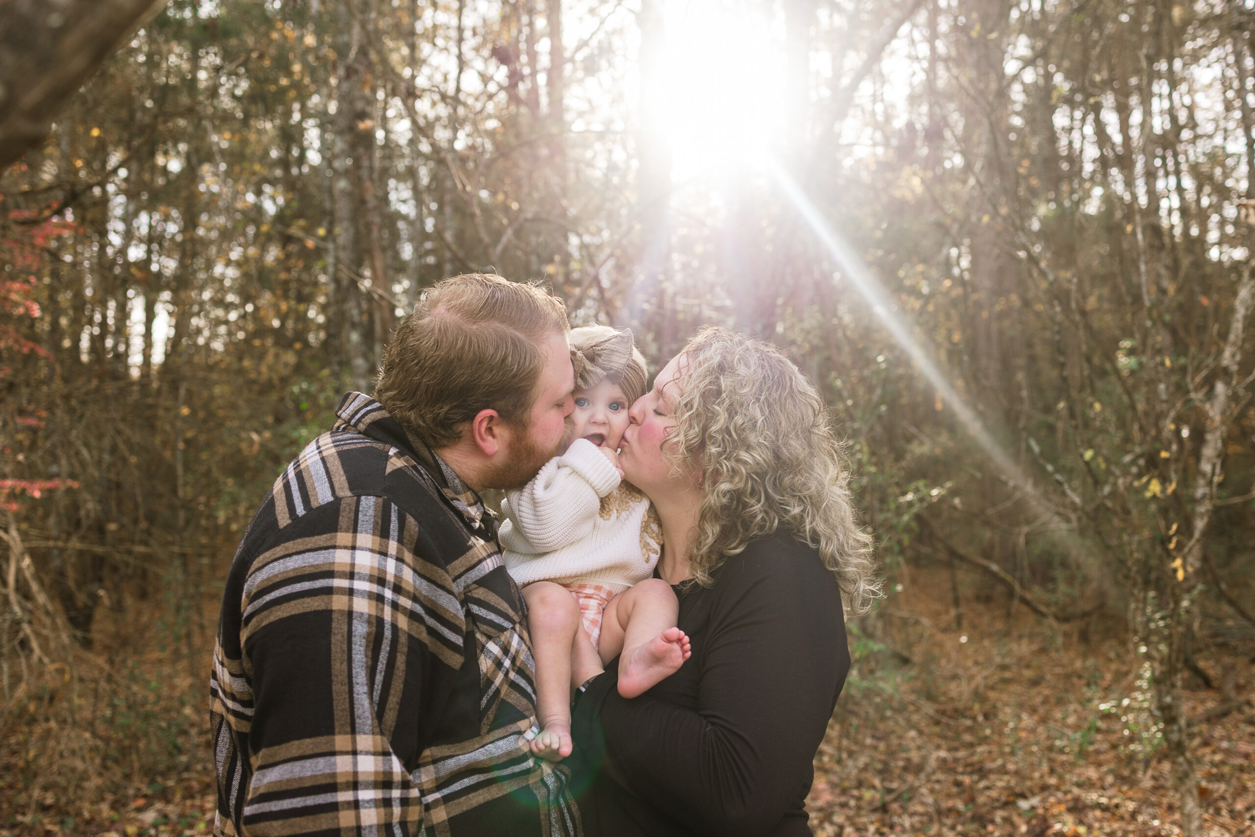 a mom and dad hold their baby girl in between them as they both kiss her cheeks and squich her cute face, the baby is stunned.